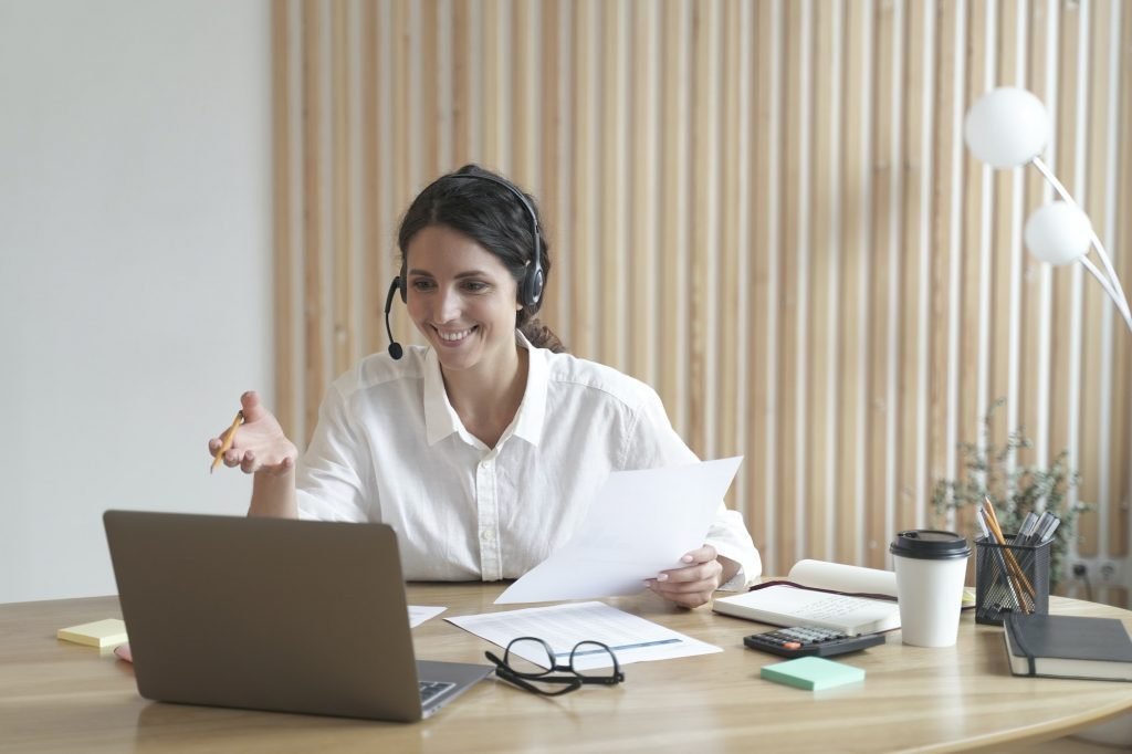 Happy italian female tutor in headset conducts webinar online on laptop in modern home office