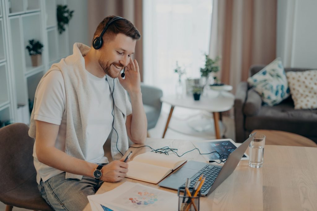 Smiling man using headset and notebook while learning online